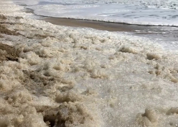 Sea foam filled with sewage on a sandy beach.